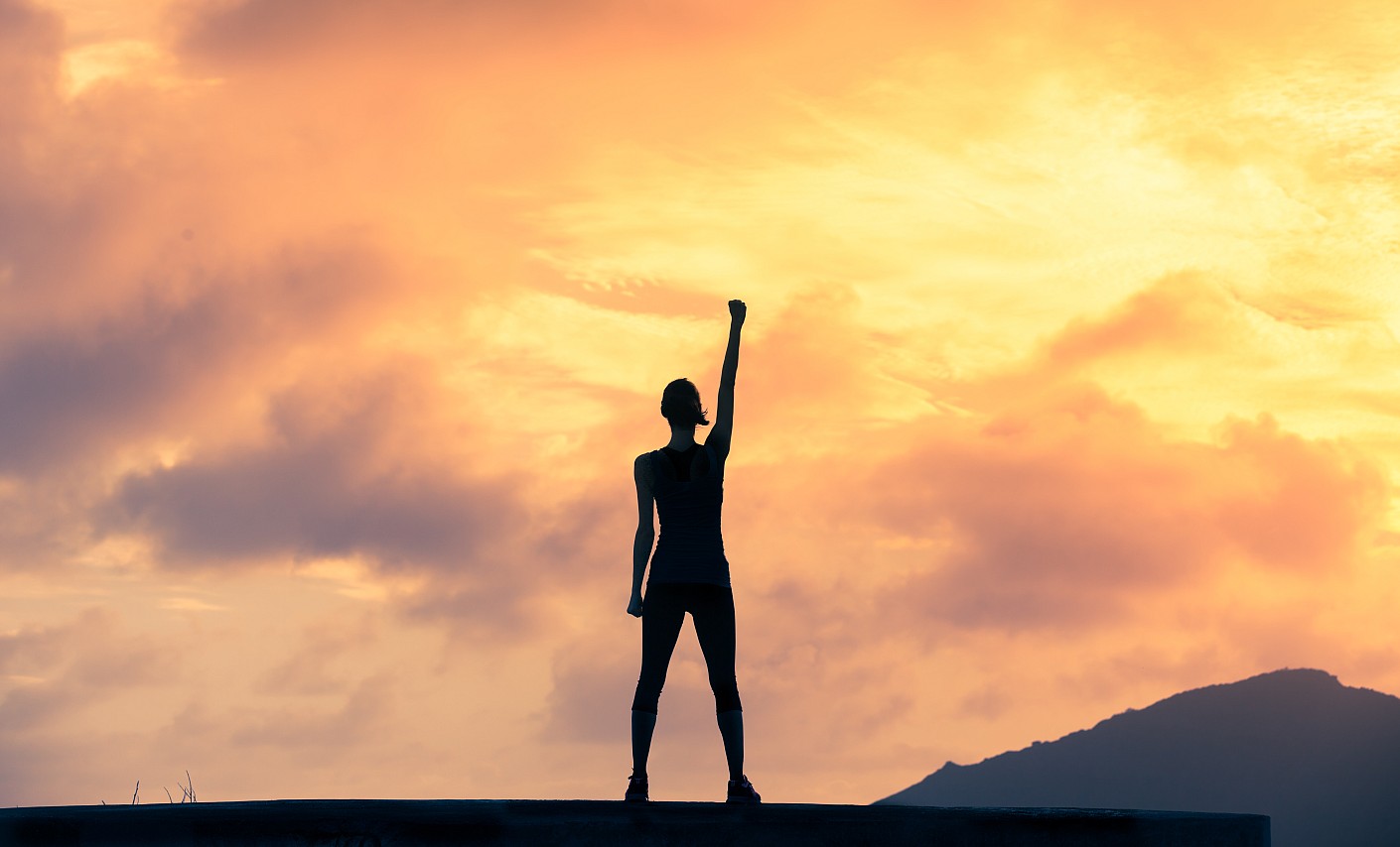 Frau vor Sonnenuntergang hebt die Faust