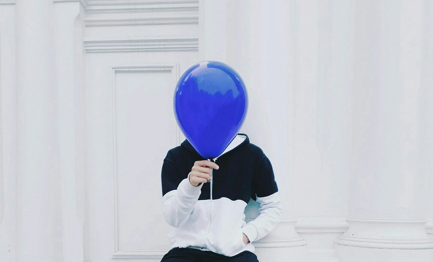 Mensch verdeckt Gesicht mit Ballon